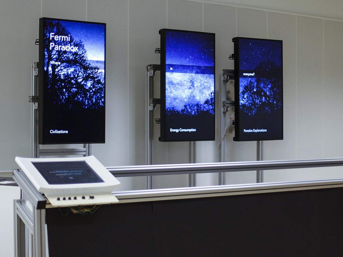 Fermi Paradox exhibition setup with three monitors in the background and a movable shift screen in the foreground.